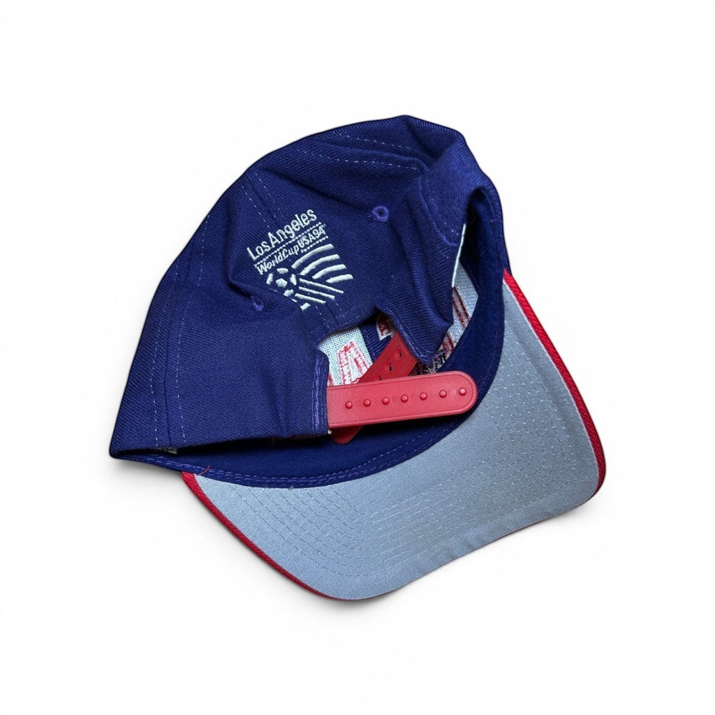 ACOLDWASH blue snapback cap with red brim and grey underside, featuring "Los Angeles WorldCup USA 94" embroidery.